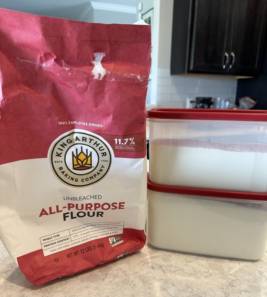  Image of an empty flour paper bag and 2 sealed containers of flour to demonstrate how long will flour last in a sealed container.
