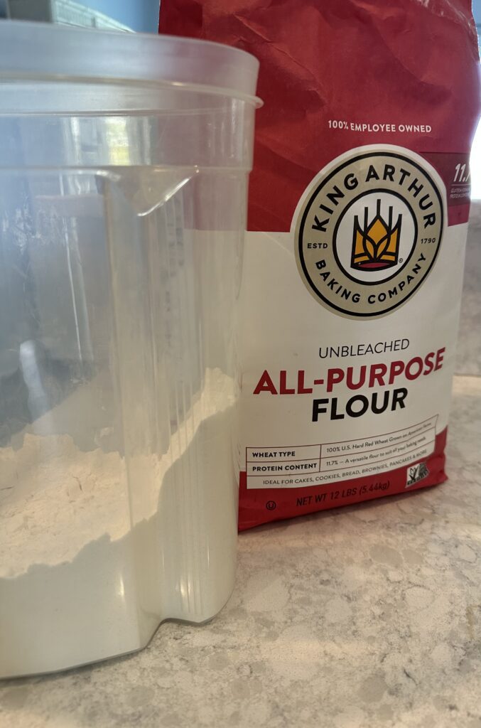 Image of a plastic container of flour next to the a full bag of flour.