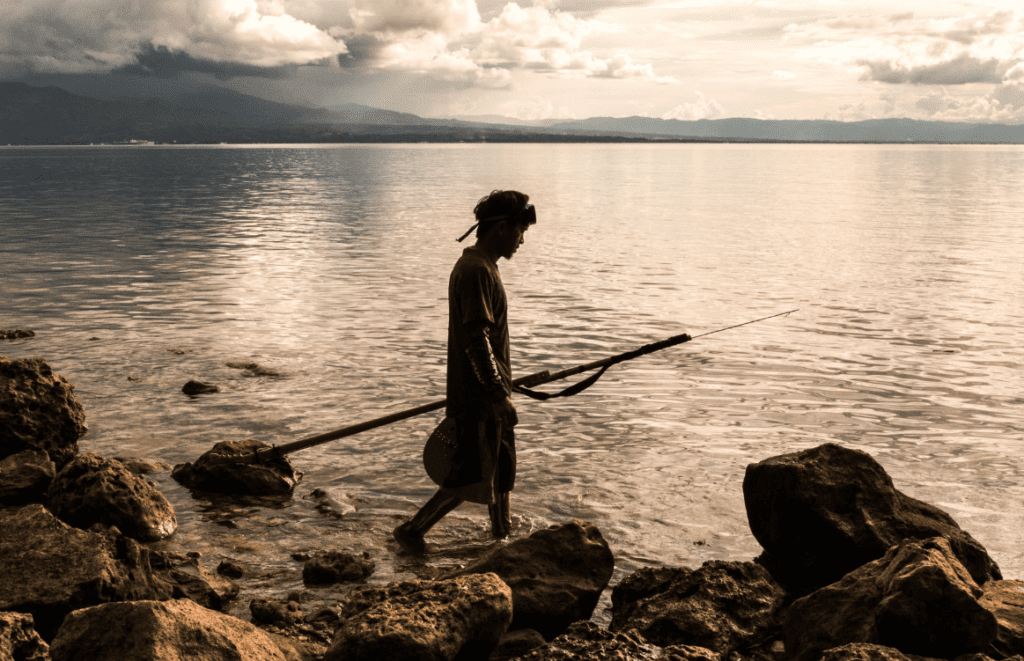 Photo of a person spear fishing along the waterline.