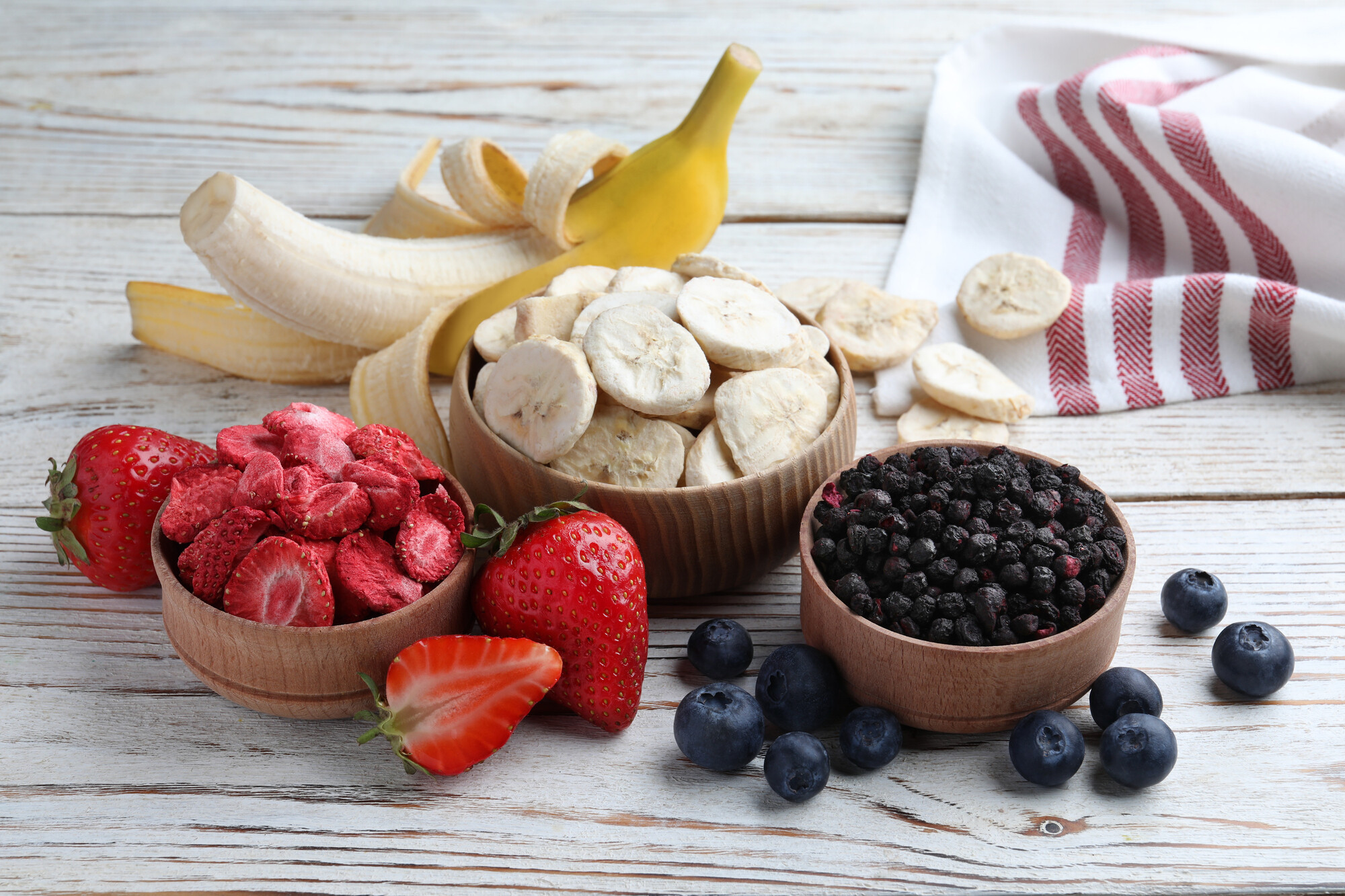 Freeze dried bananas, strawberries and blueberries next to fresh bananas, strawberries and blueberries made with one of the best freeze dryers.