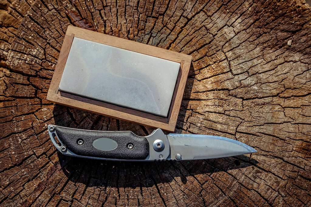 Photo of a survival knife sharpener on a log. next to a knife.