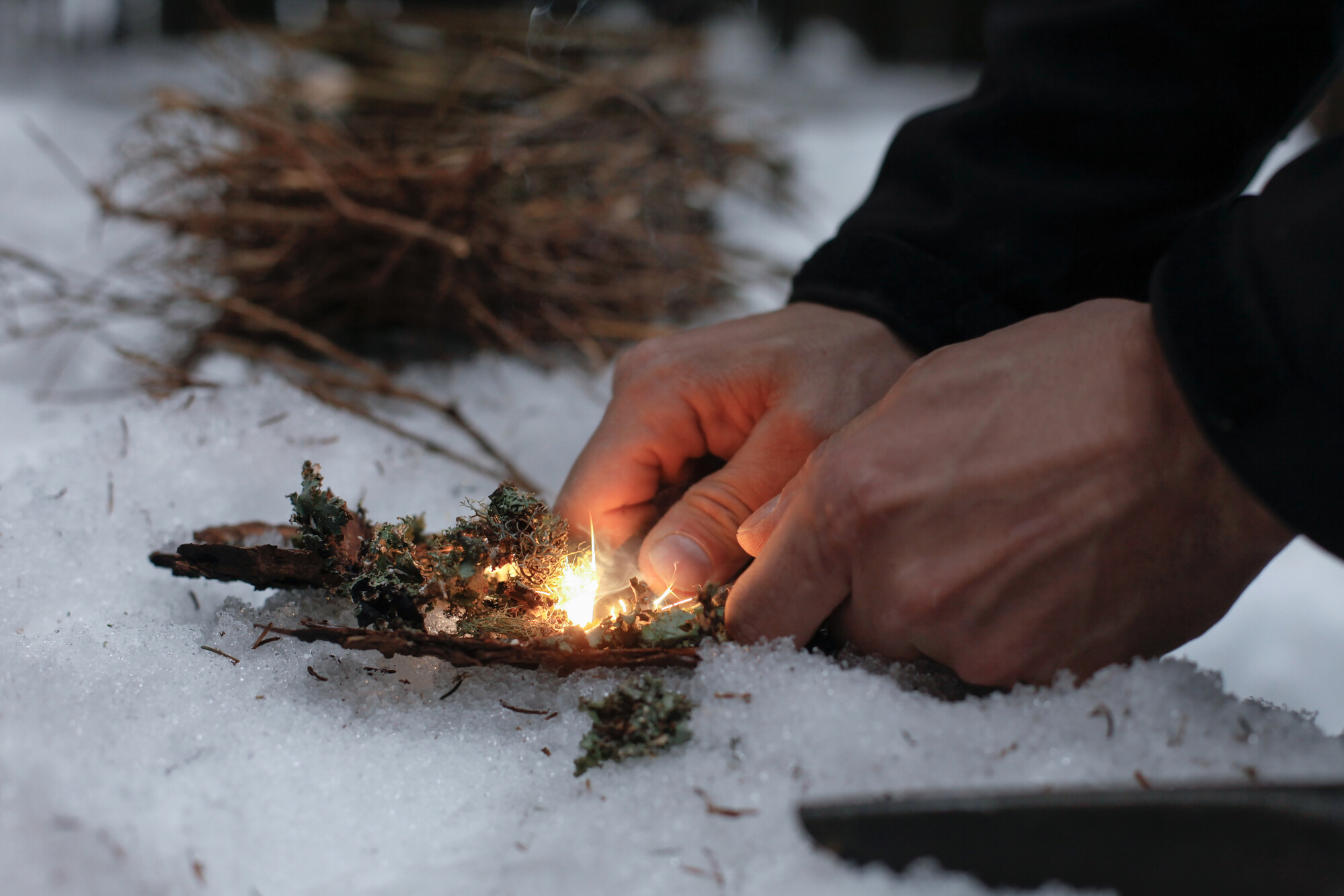 Photo of a person starting a fire in the snow using a fire starter.