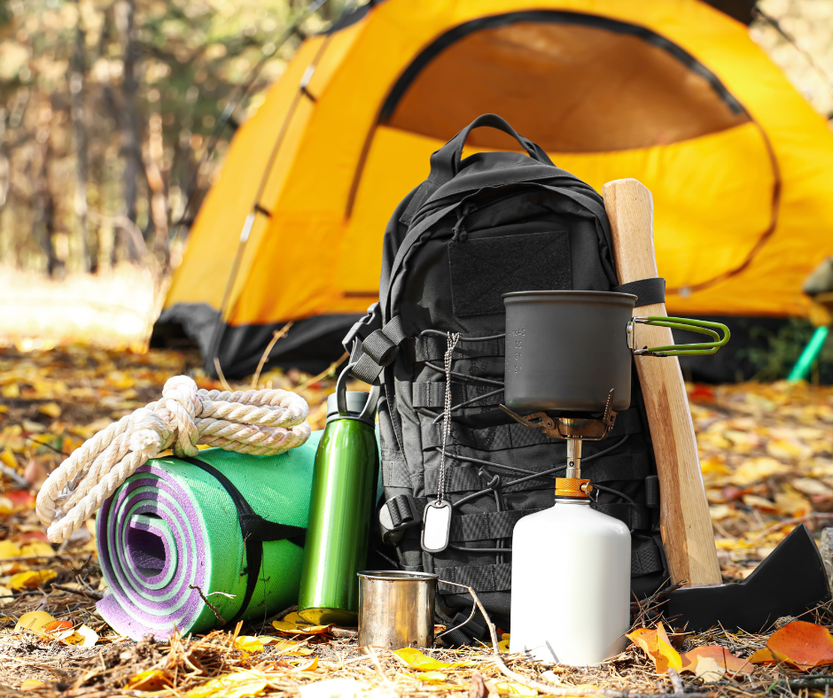 Photo of survival gifts at a campsite, including a tent, backpack, camp stove, water bottle, axe, cookware and bedroll.