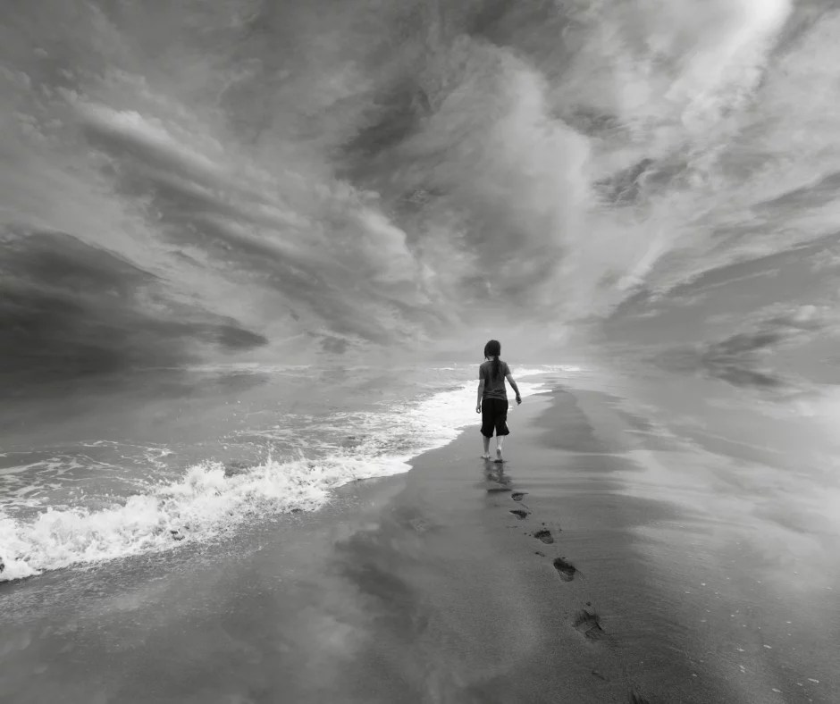 Black and white photo of a child walking on a beach with footprints in the sand motivation to keep going.
