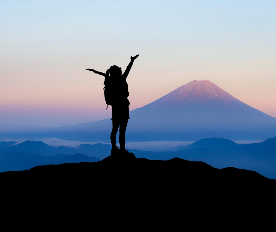 Photo of a woman motivated to climb a mountain. She stand at the top arms wide open.
