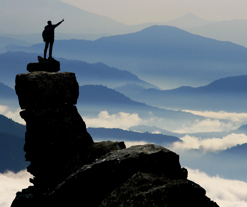 Photo inspiring us to climb to the top and persevere. A man standing at the top of a mountain holding up 1 finger.